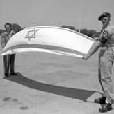 Held by a Haganah military policeman and an unidentified Jewish official, the flag of the newly proclaimed Jewish state of Israel.